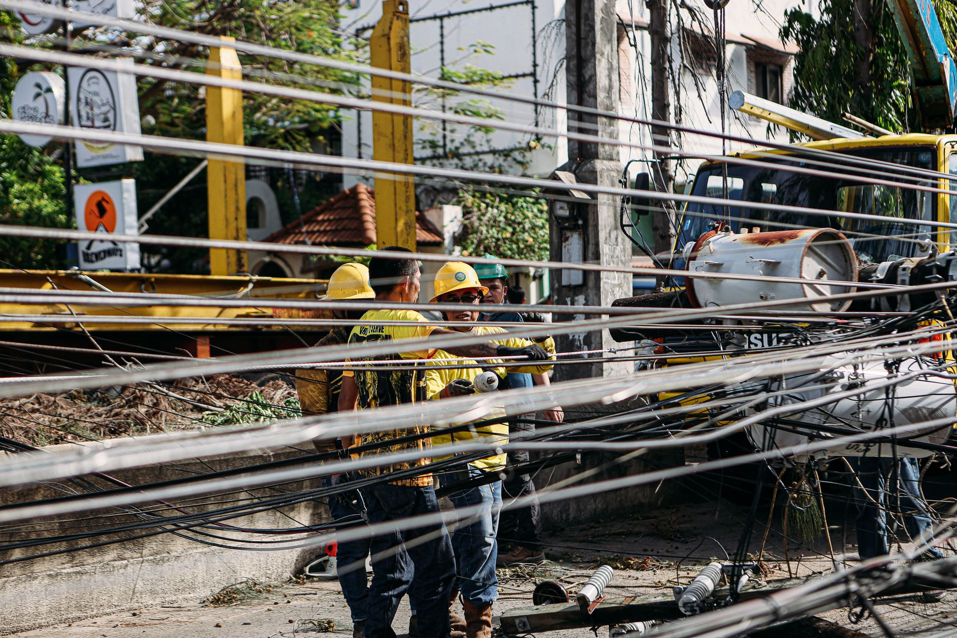 Utility workers repairing downed power lines amidst damaged infrastructure. Outdoor setting with chaos.