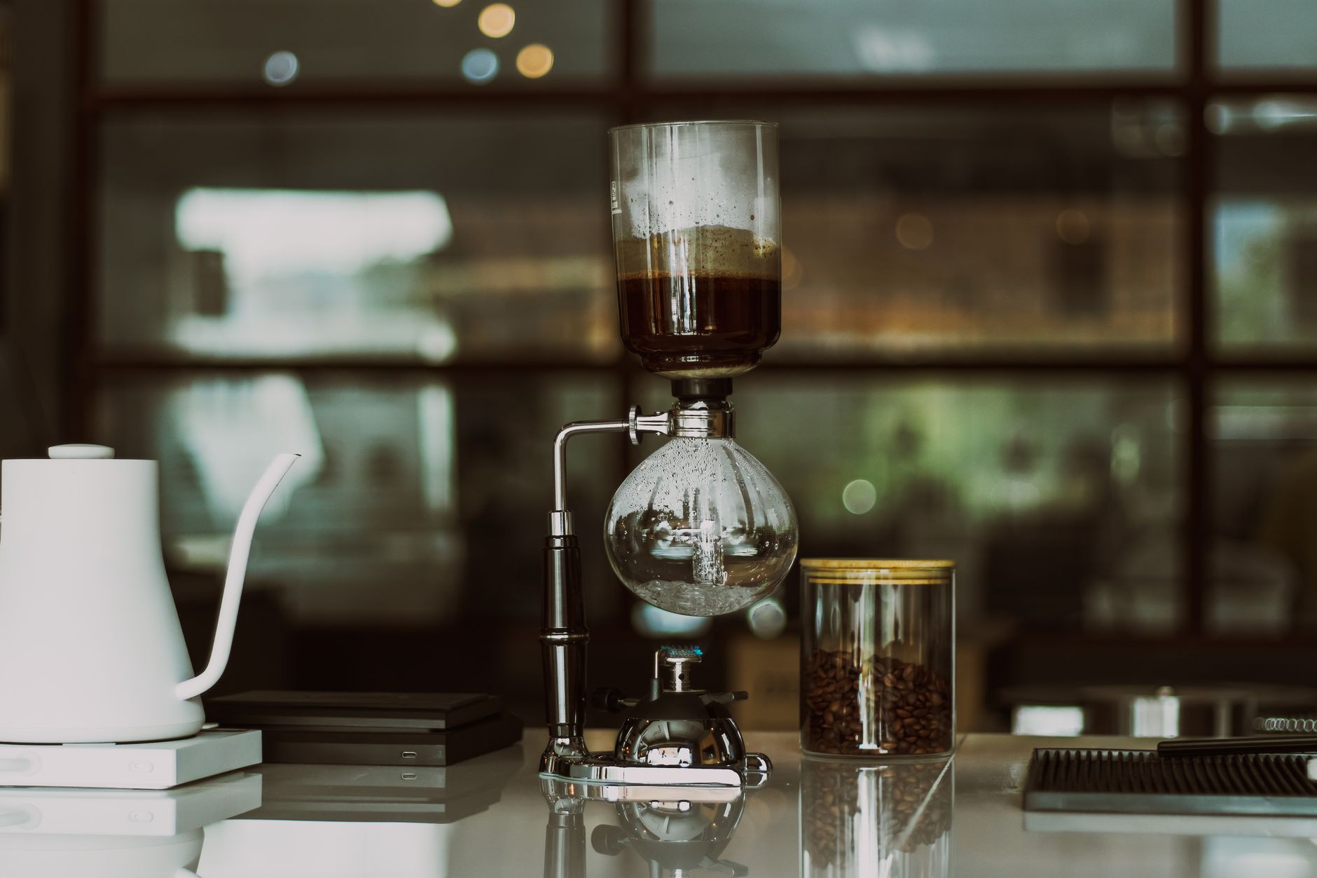 A sleek siphon coffee maker setup with kettle and coffee beans on counter.