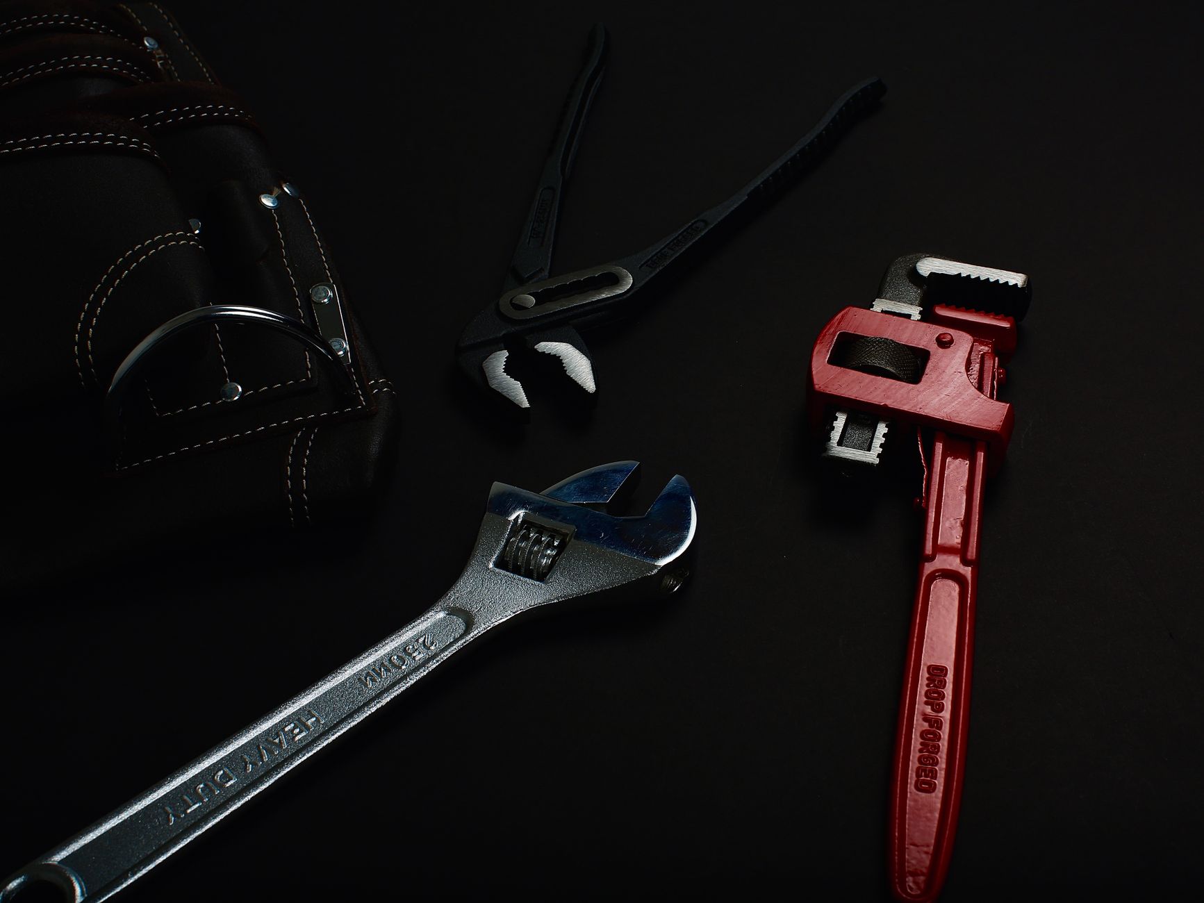Close-up of various hand tools including wrenches and pliers on a dark surface.